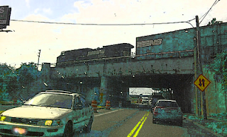 View of a riveted steel overpass in a rust-belt town under hazy sun